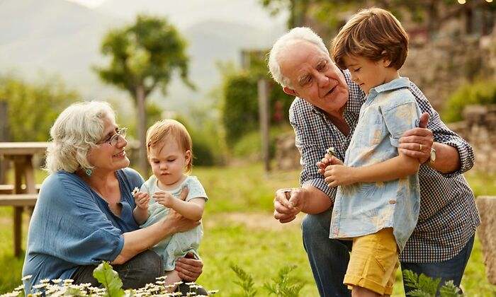 Un abuelo y una abuela jugando en el jardín con sus dos nietos, uno de seis y otro de un año