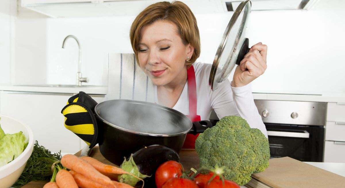 Una señora abre una olla y se detiene a olerla con cara de satisfacción