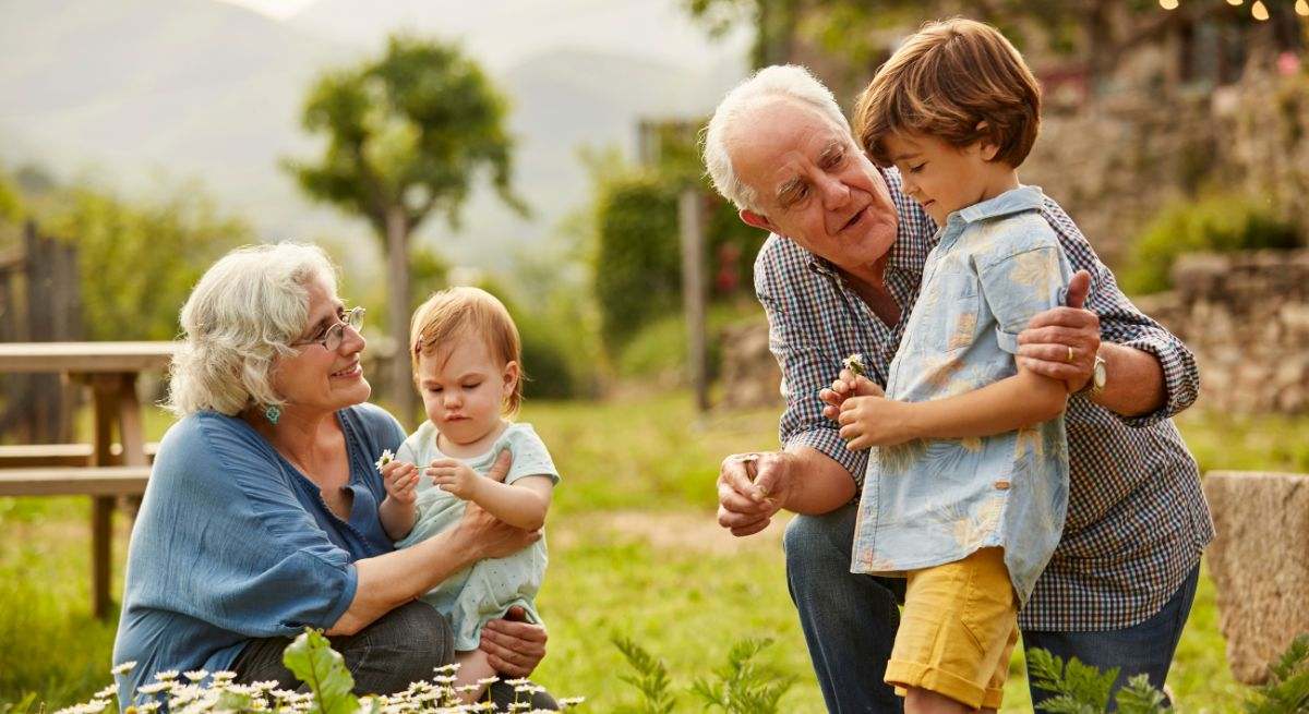 Un abuelo y una abuela jugando en el jardín con sus dos nietos, uno de seis y otro de un año