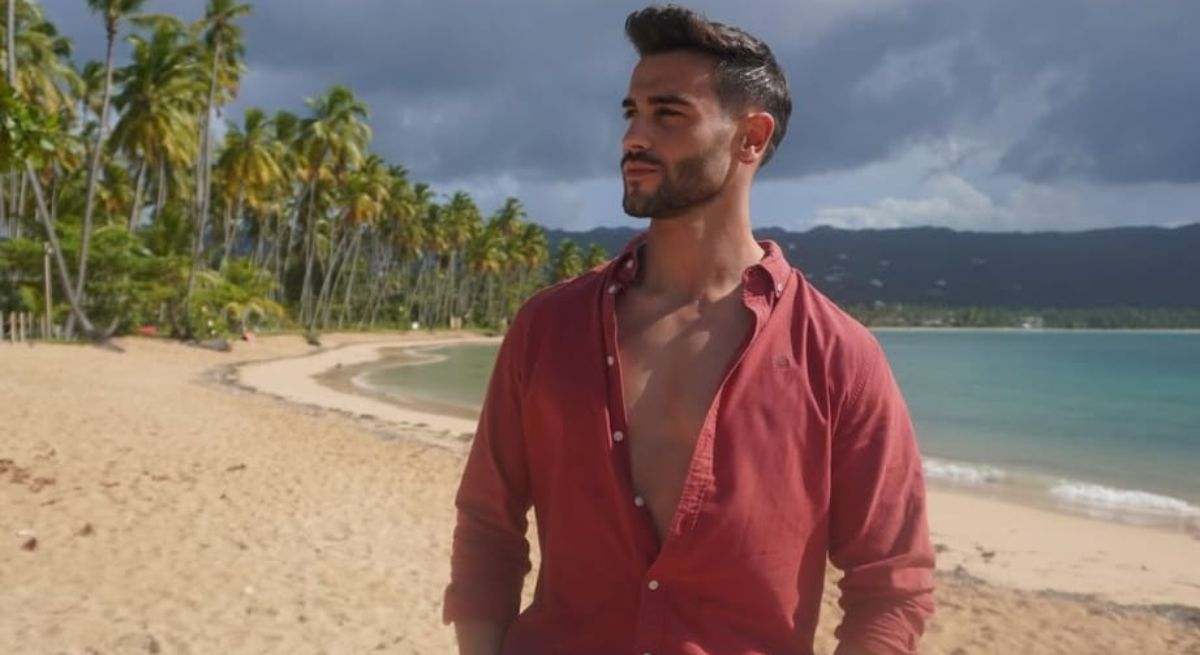 Gerardo posando en la playa con camiseta rosa abierta 