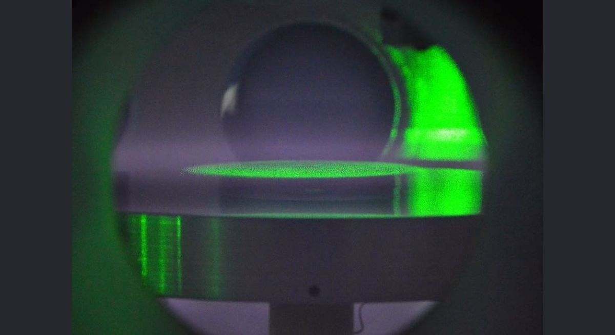 Una vista dentro de la cámara de vacío del laboratorio, donde las partículas coloidales están suspendidas en un disco plano, iluminado por la luz verde de un láser, para estudiar el plasma polvoriento. / Foto: EP