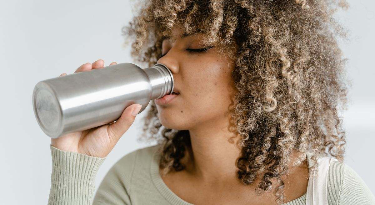 Chica con pelo rizado bebiendo de una botella de metal