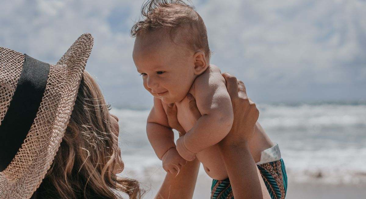 Una madre con un sombrero levantando a su bebé en la playa