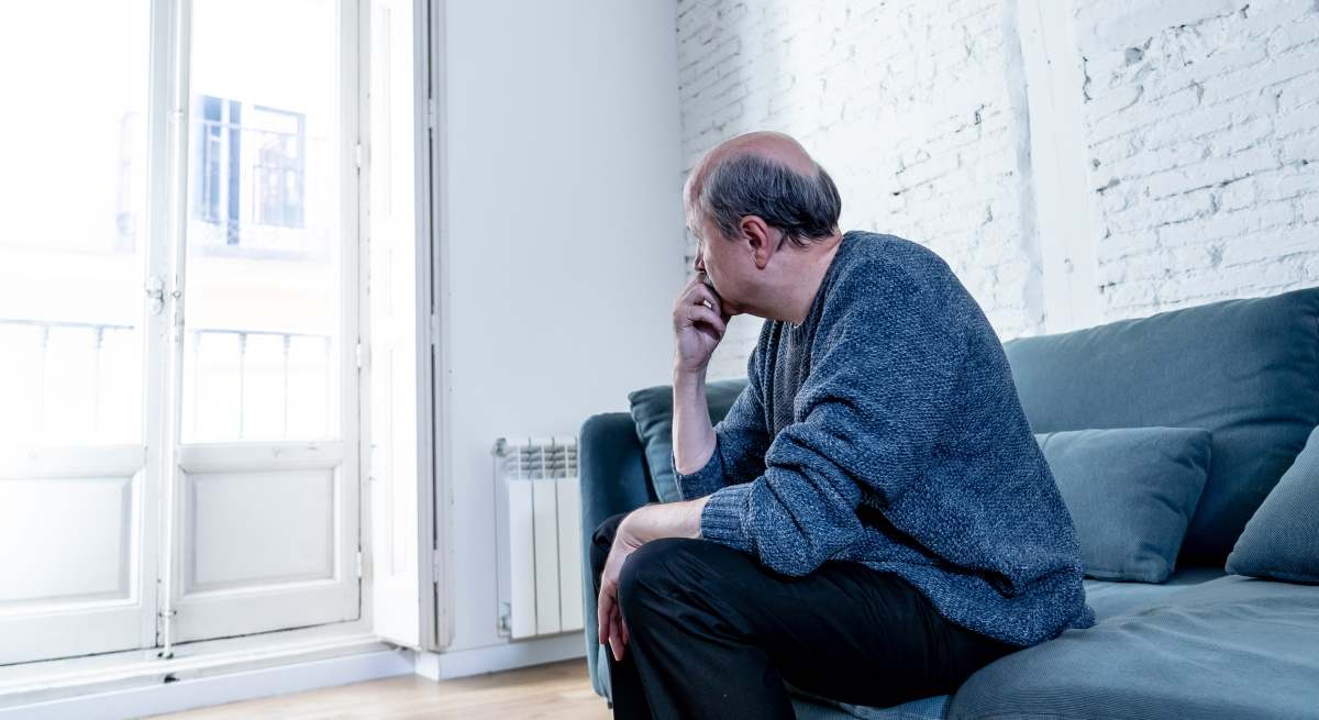 Un jubilado sentado en su sofá mira a la ventana.