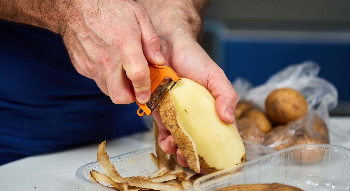 Un hombre pelando una patata con un pelador naranja