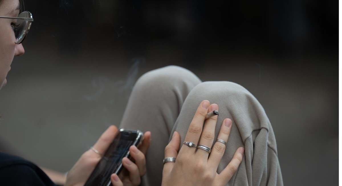Una joven fuma y lee su movil en las inmediaciones del colegio Pia Balmes.
