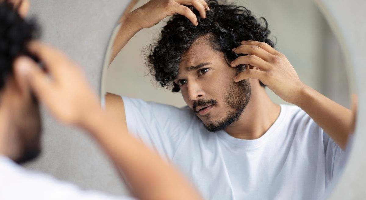 Hombre joven con el pelo negro mirándose al espejo para ver si tiene canas