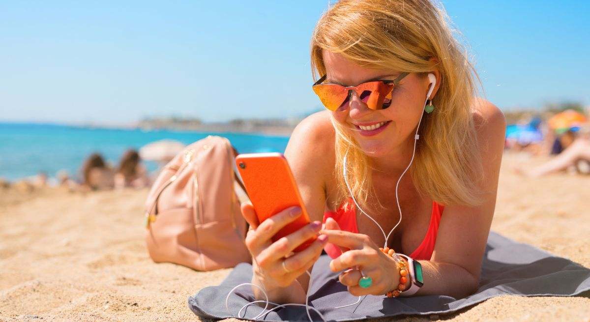 Una mujer descansa plácidamente en la playa, con su teléfono móvil