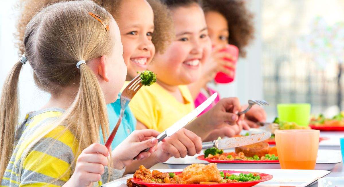 Varios niños comen su plato principal con una sonrisa