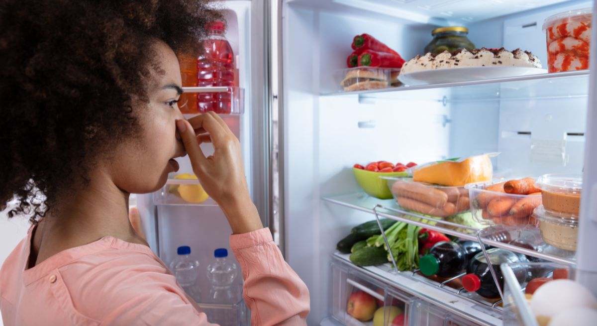 Chica se tapa la nariz porque hay alimentos en mal estado en la nevera