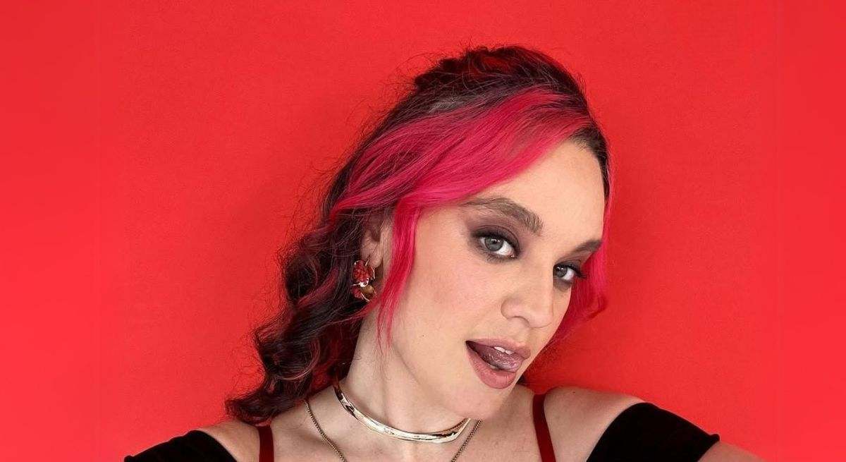 La cantante con un mechón de pelo rojo posando en un fondo rojo