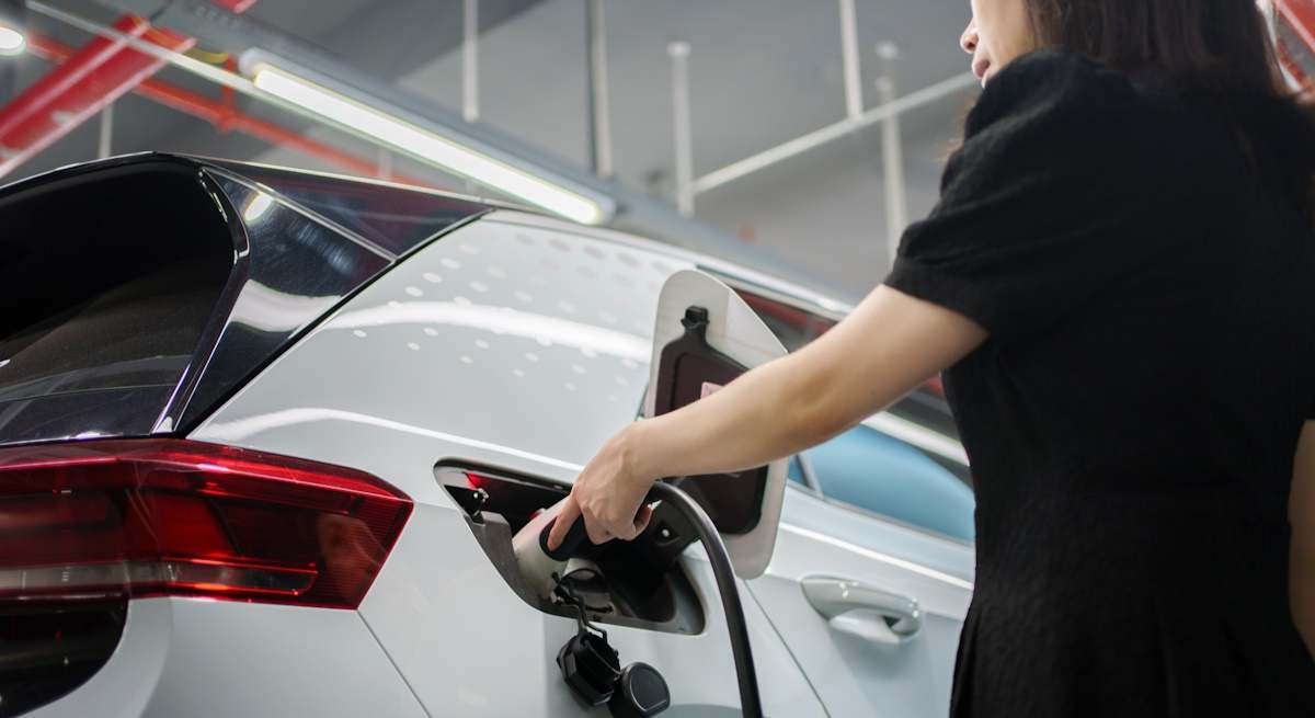 Una mujer asiática recarga su coche eléctrico. | iStock.