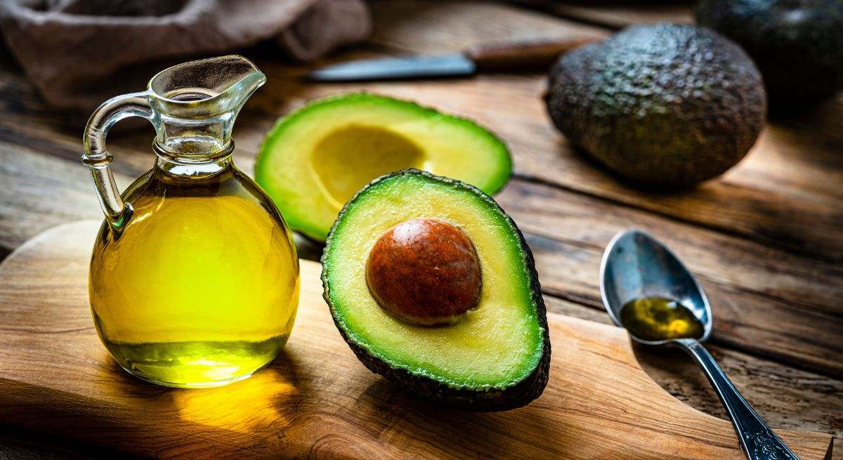 Aguacate partido por la mitad sobre una tabla de madera y junto a una jarrita llena de aceite