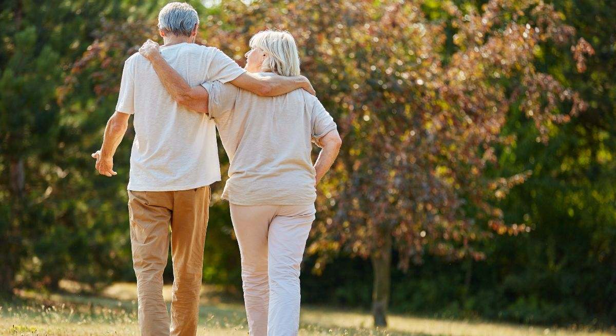 Dos personas de avanzada edad se abrazan mientras pasean por un parque