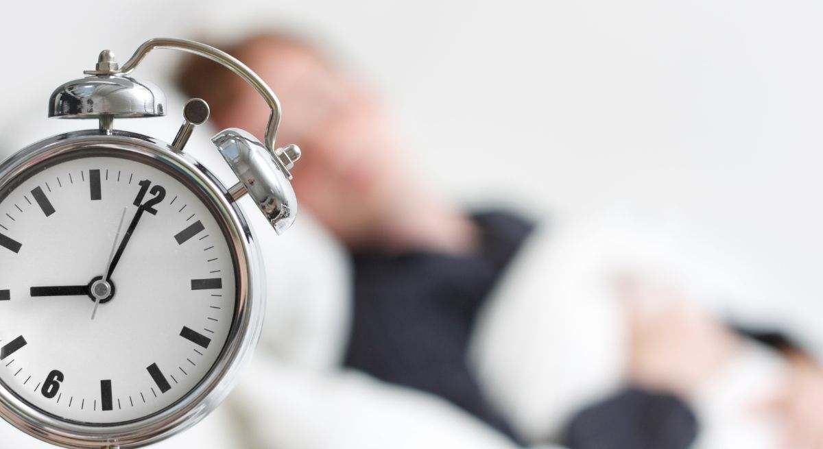 Un reloj despertador y una chica durmiendo de fondo