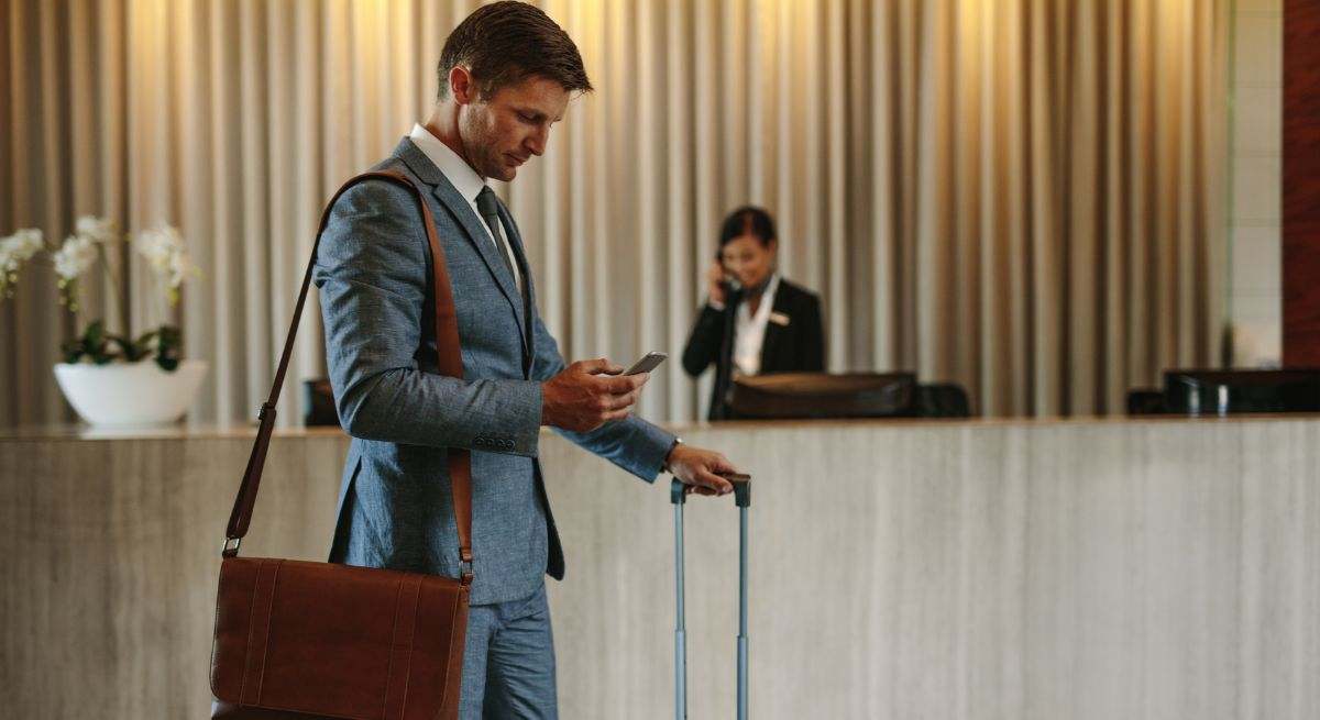 Un hombre trajeado entra a una recepción de hotel con la maleta en la mano
