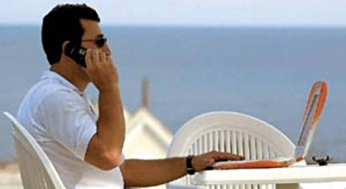 Un hombre ante un portátil habla por teléfono en la playa