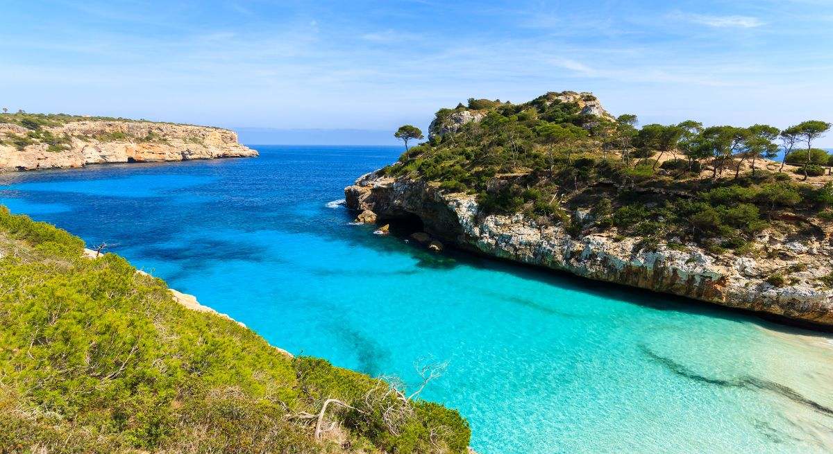 Una playa paradisíaca en Menorca con aguas cristalinas y bordeada por acantilados repletos de vegetación.