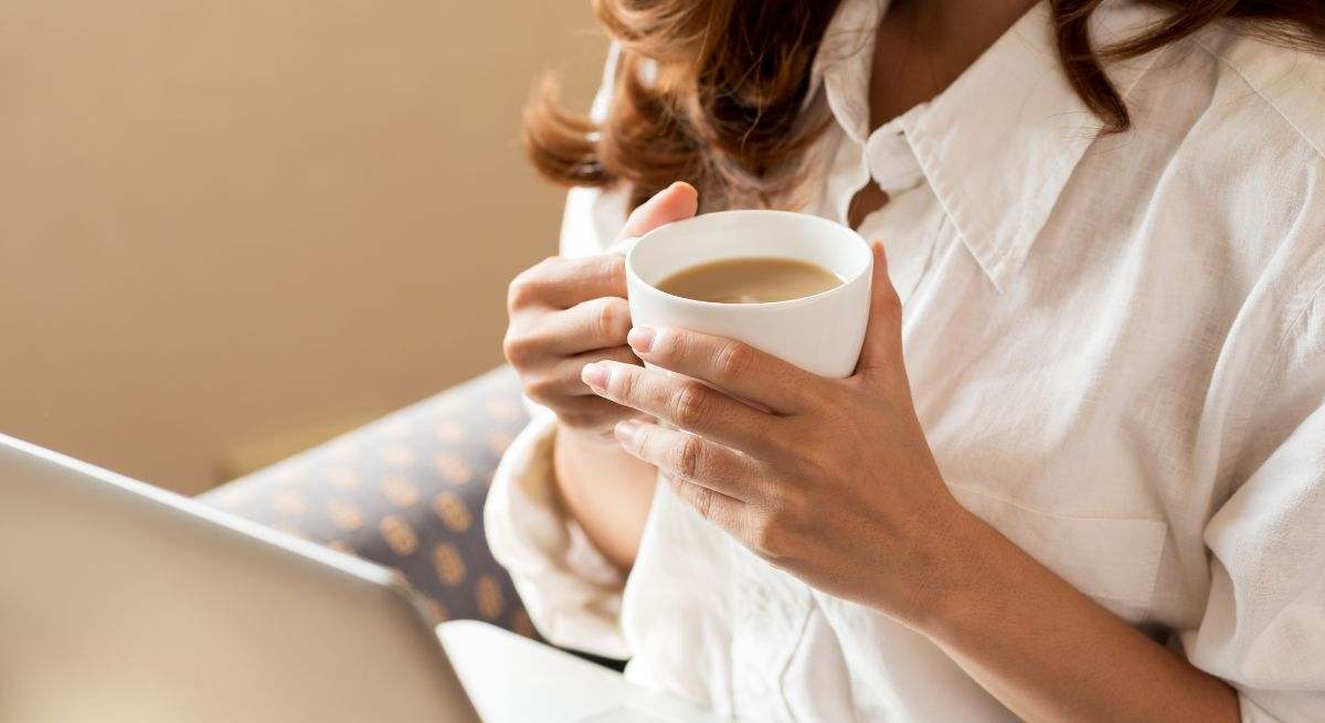 Una mujer bebé café en su casa, mientras trabaja con el ordenador 