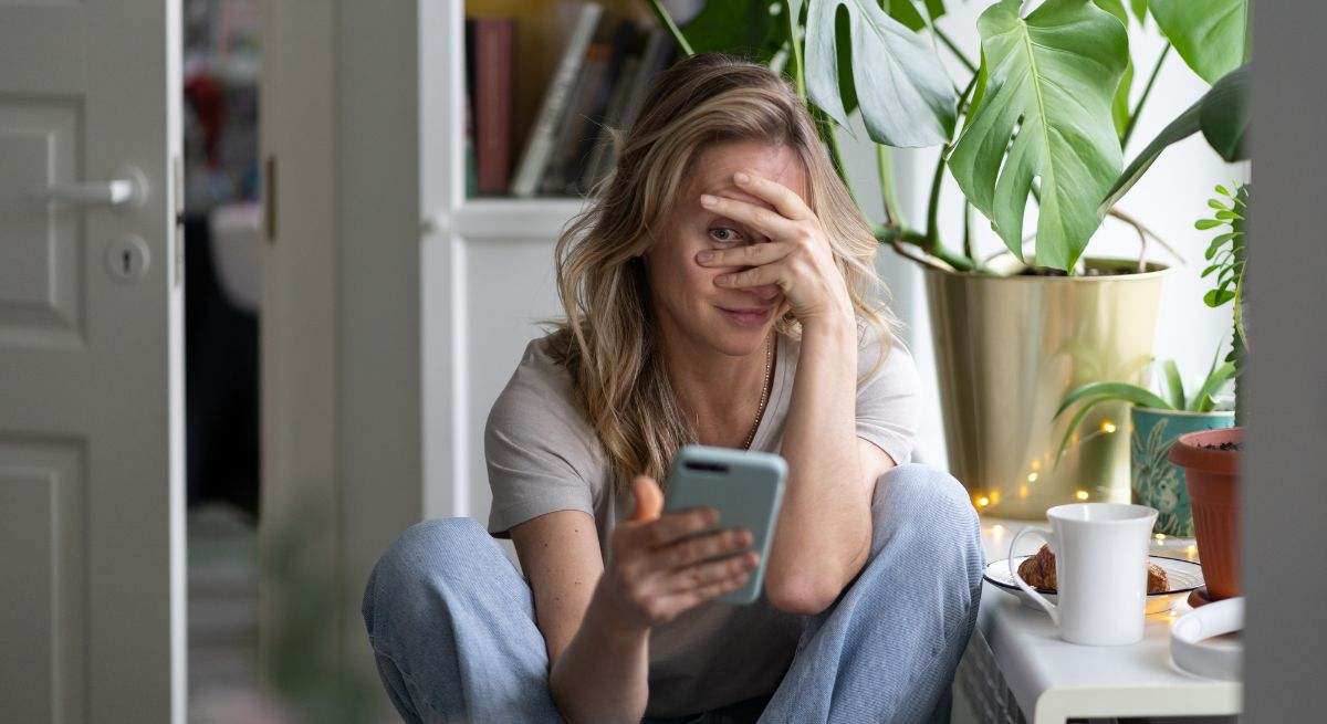 Mujer mirando el teléfono y tapándose la cara con una mano