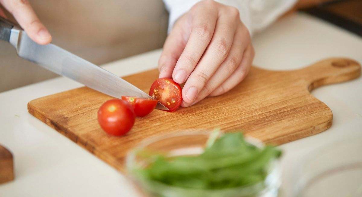 Una persona corta un tomate en una tabla de madera