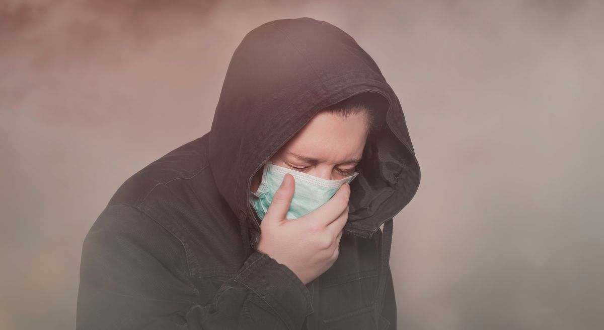 Hombre tosiendo con mascarilla en un ambiente contaminado