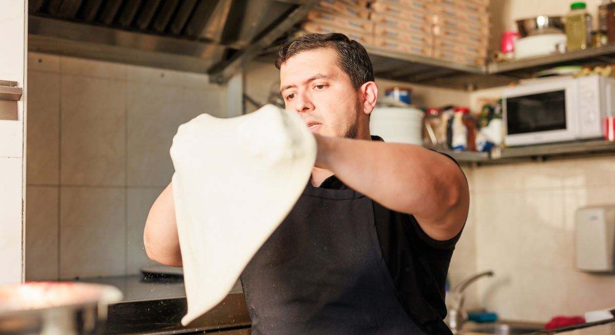 Un pizzero amasando la pizza en su local