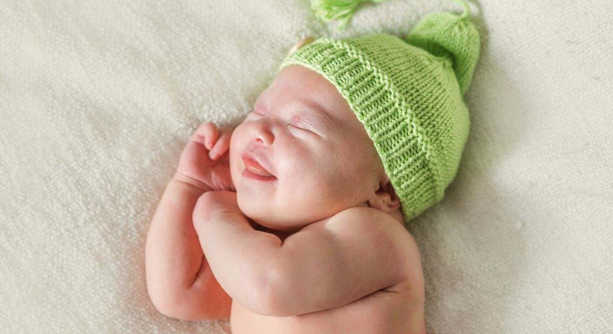 Un recién nacido duerme en su cama con una gran sonrisa