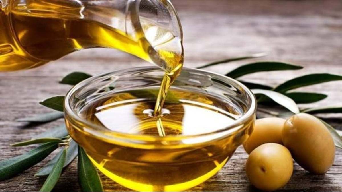 Aceite de oliva servido en un cuenco de cristal al lado de unas aceitunas y una hoja de olivo