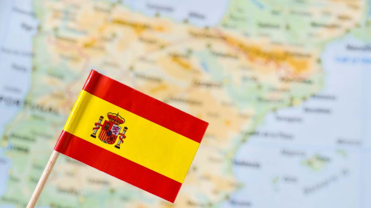 Una bandera de España encima de un mapa difuminado del país.