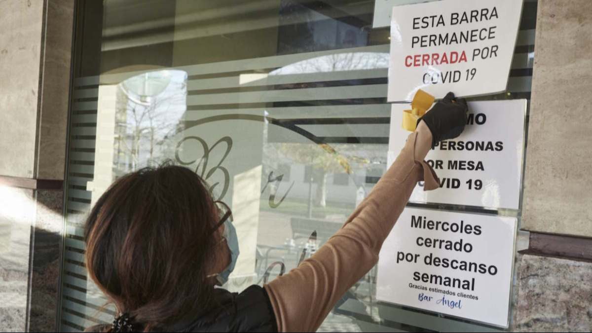 Empleada de un bar colocando carteles con restricciones durante la pandemia