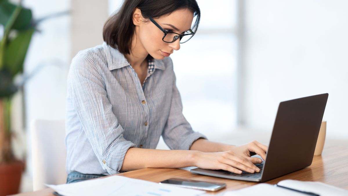 Una mujer con gafas, concentrada en su trabajo con un ordenador. 