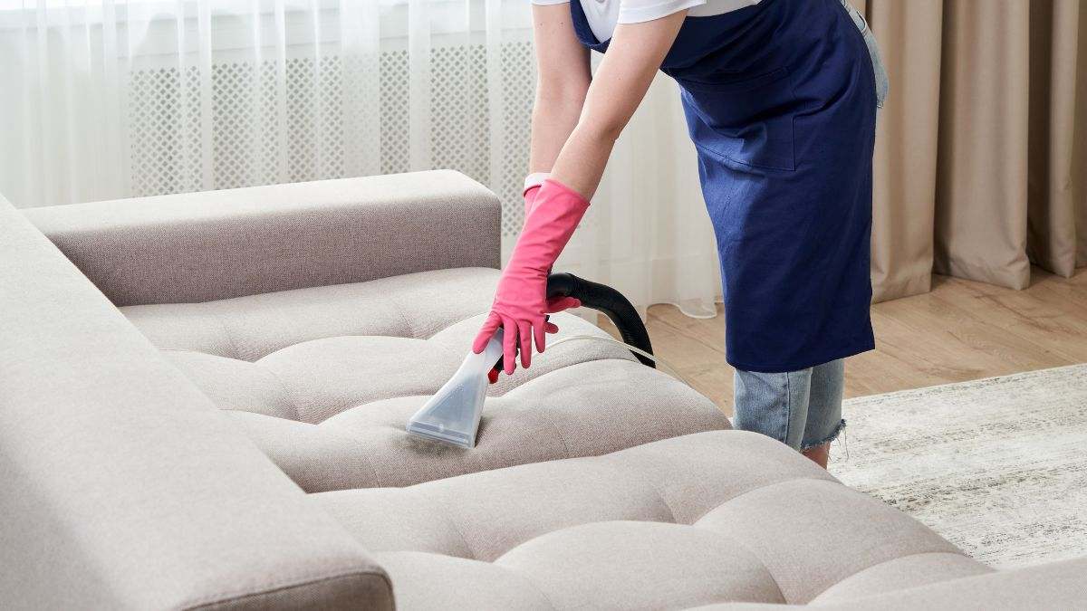 Una empleada de hogar limpia el sofá de una casa.