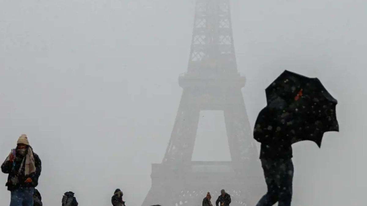 Varias personas caminan cerca de la torre Eiffel mientras nieva