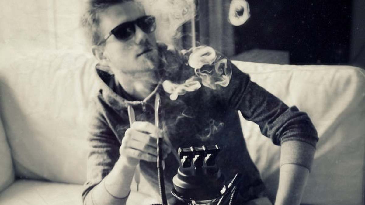 Joven con gafas de sol fumando de una cachimba sentado en un sofá