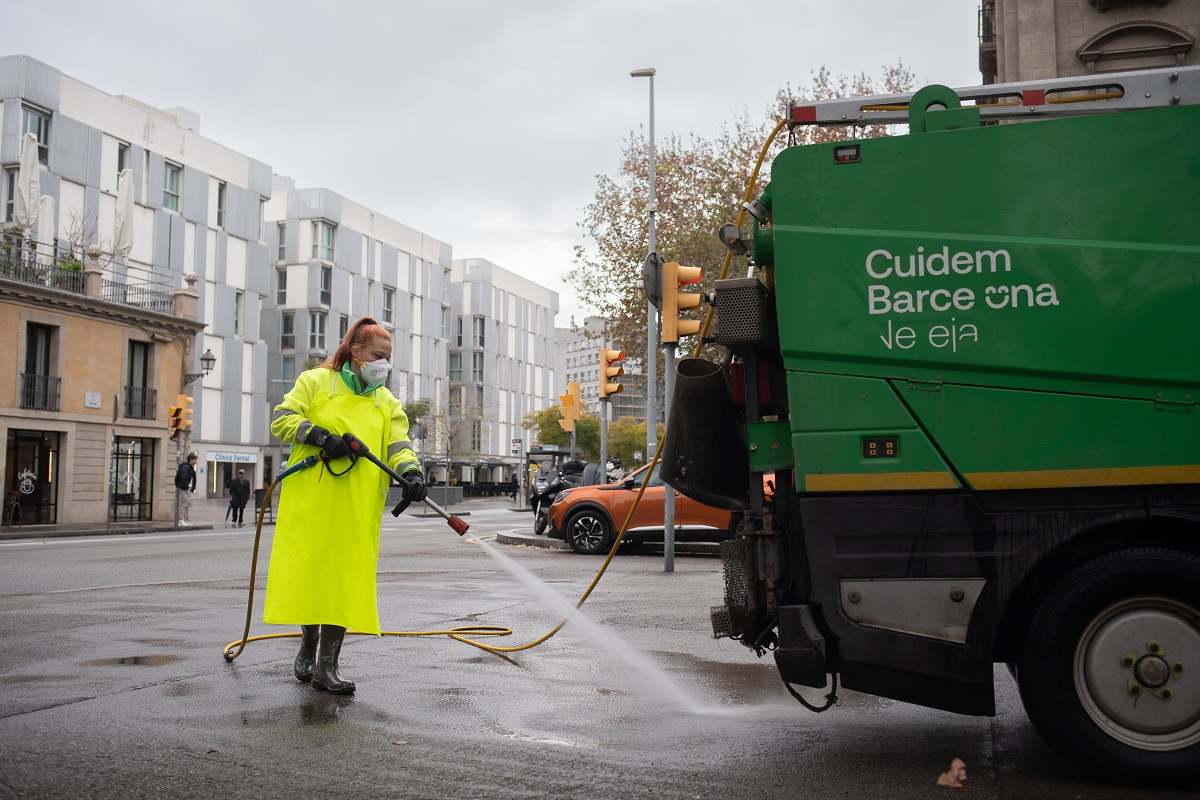 Una trabajadora de la limpieza riega una calle con una manguera en Barcelona. EE