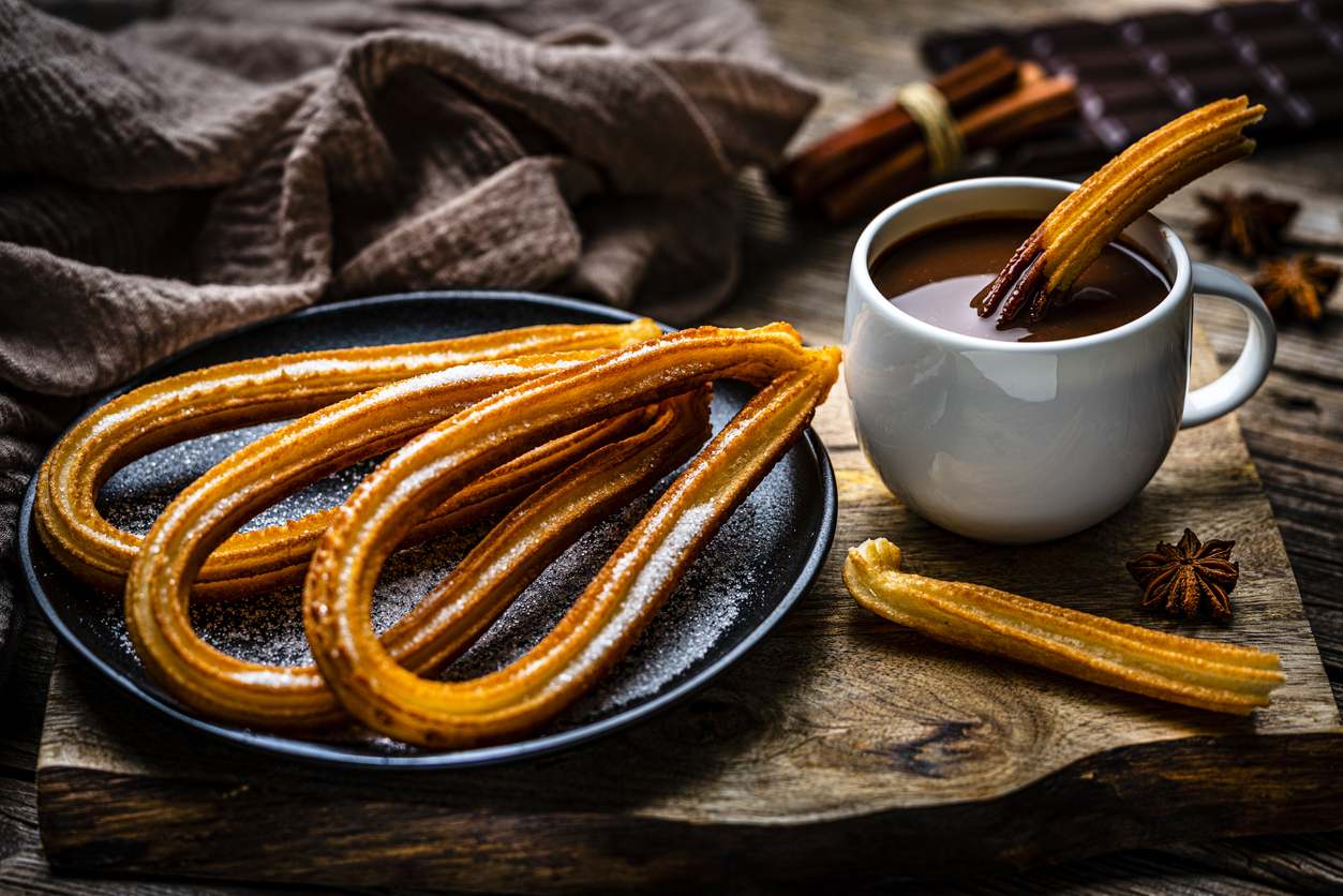 Varios churros en un plato negro y junto a una taza de chocolate