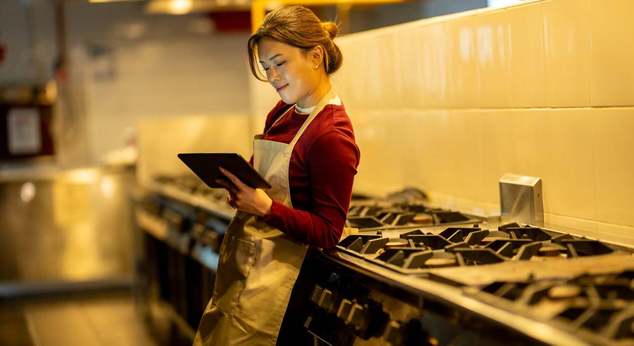 Una cocinera apoyada en los fogones mira una tablet