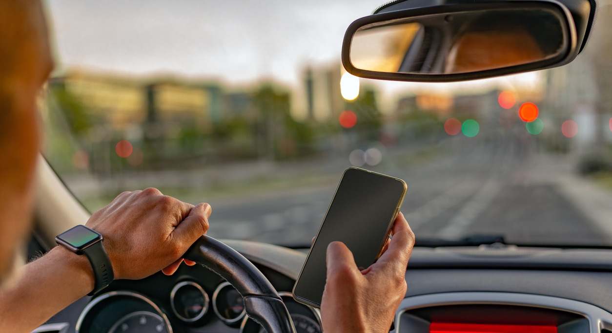 Un conductor conduce mientras consulta su teléfono móvil