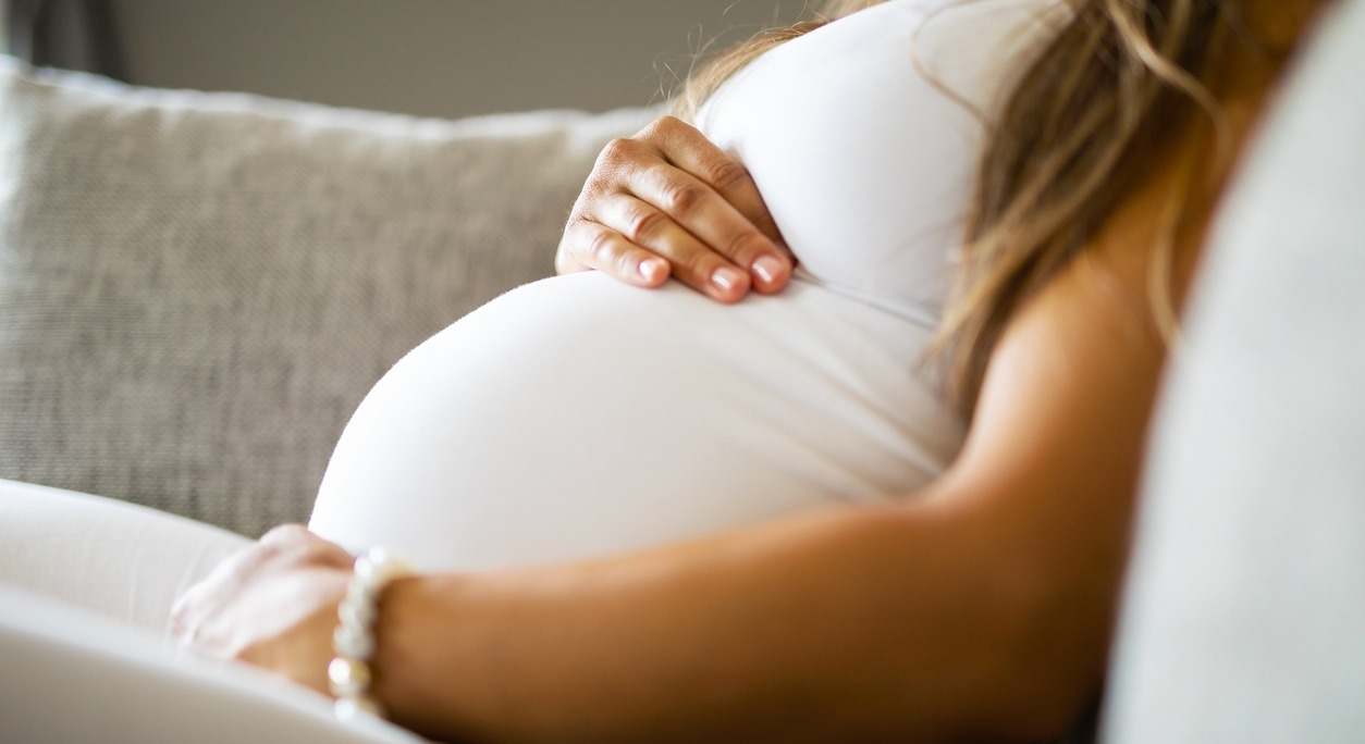 Mujer embarazada con camiseta blanca agarrando su barriga