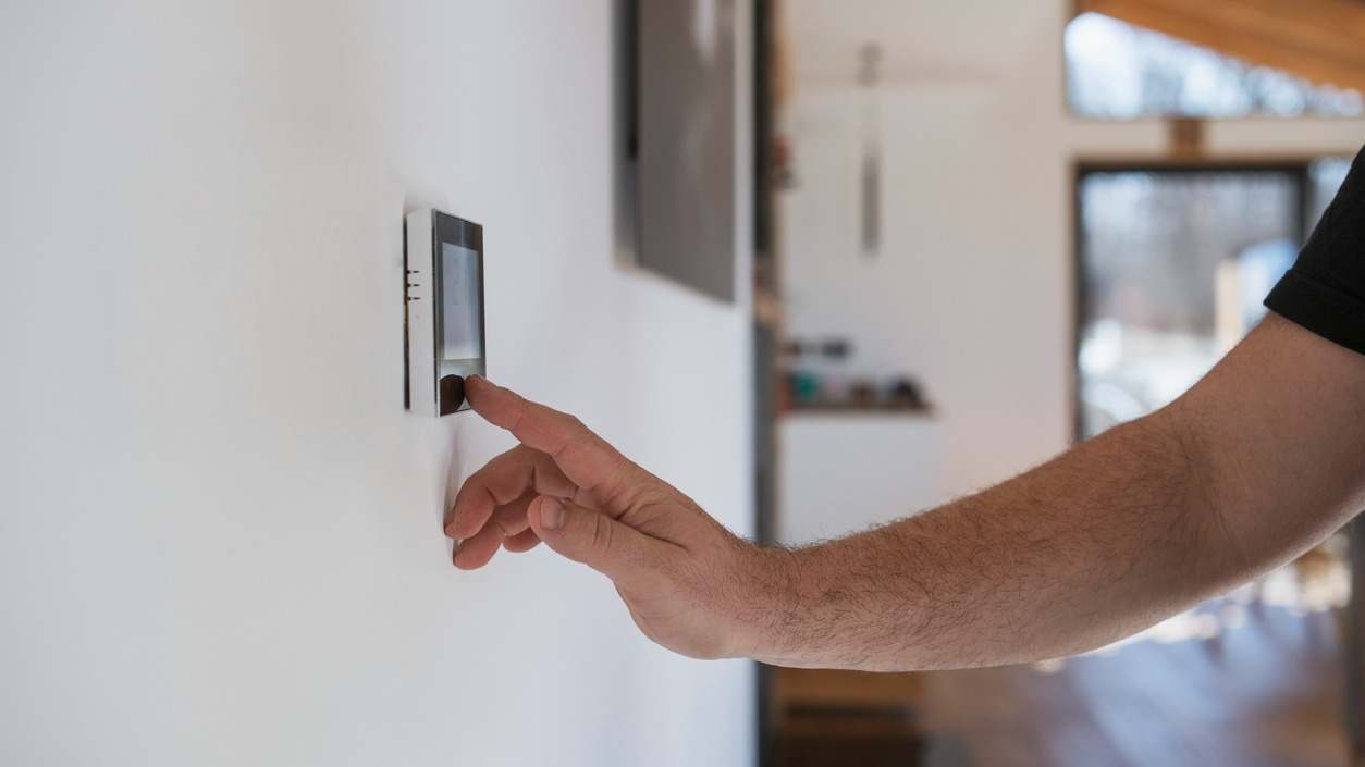 Hombre en casa ajustando termostato con dispositivo en la pared