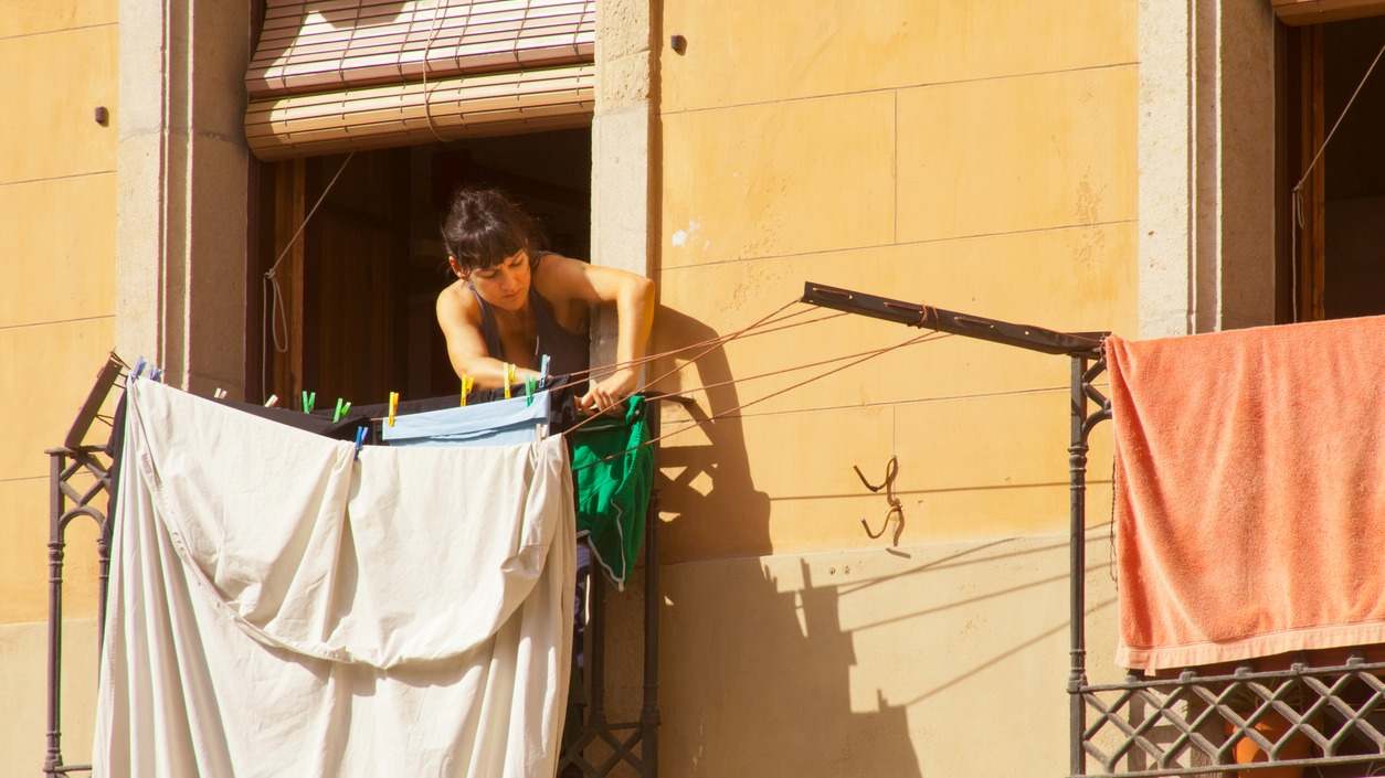 Mujer joven tendiendo la ropa en el balcón de su casa.