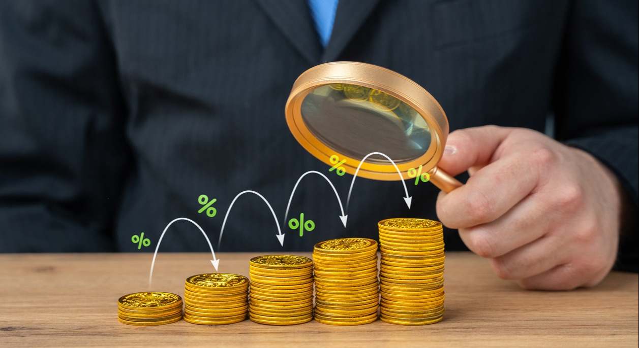 Una mano con una lupa analiza la rentabilidad del dinero. Imagen: iStock.