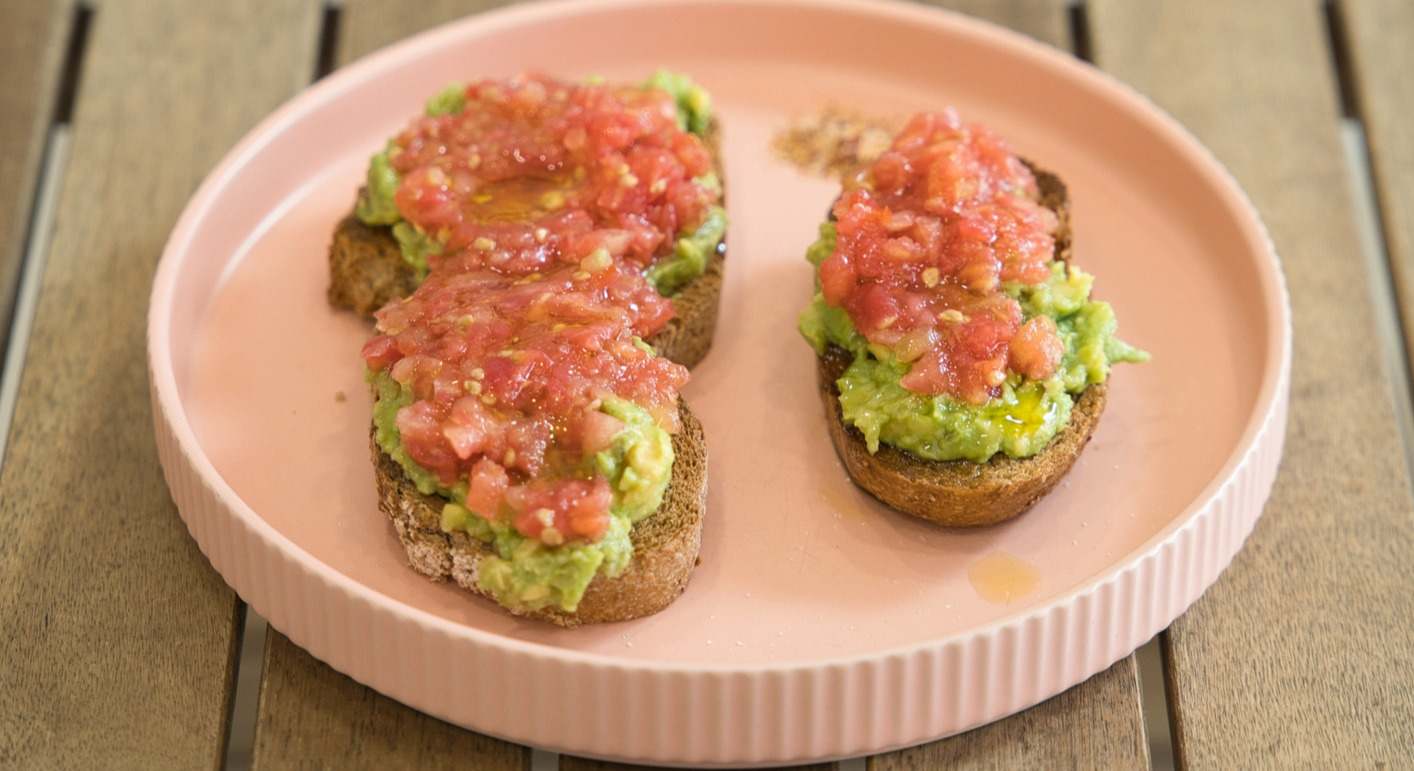 Tostadas integrales con aguacate y tomate sobre un plato rosa
