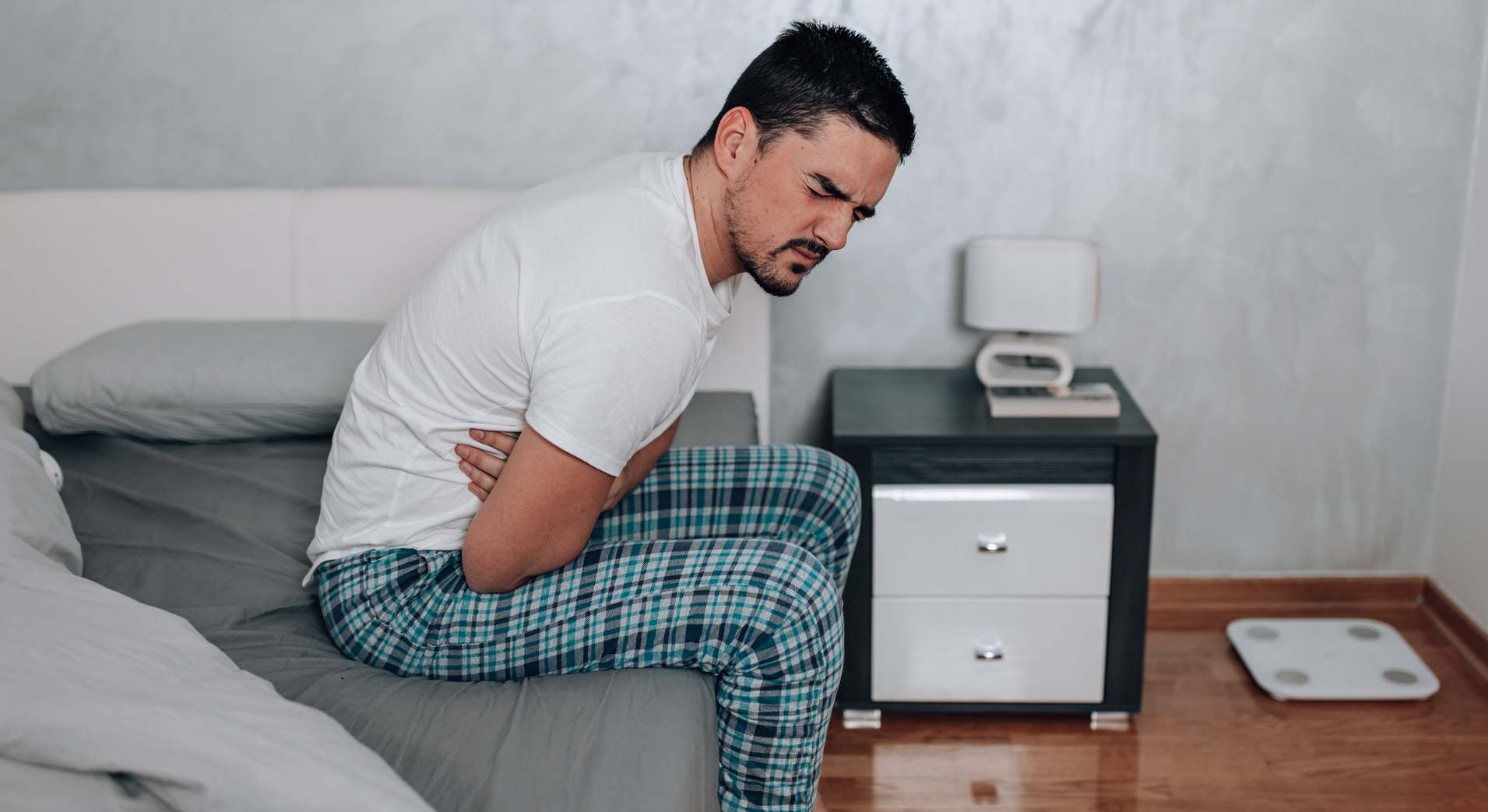 Hombre sentado en la cama con dolor de barriga