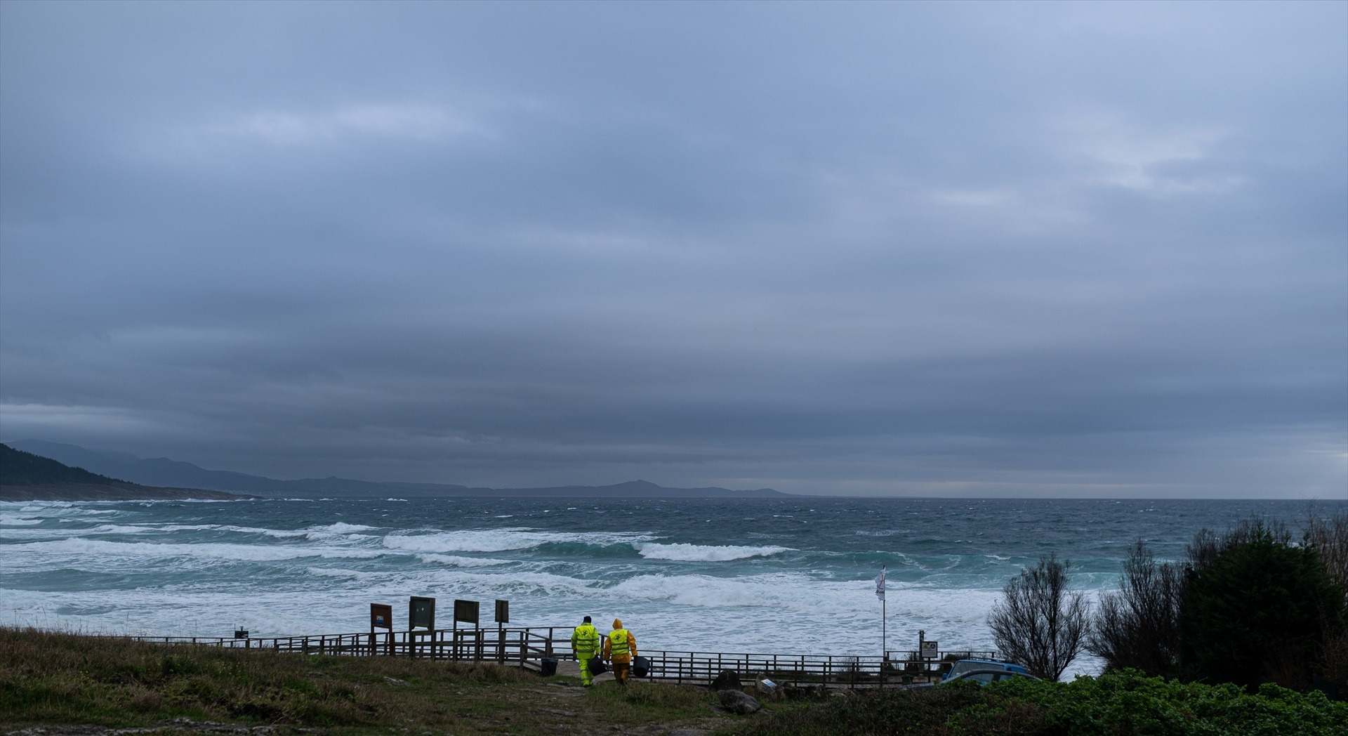 Dos hombres cargan un cubo lleno de pellets, en la playa Area Maior, en Muros, A Coruña