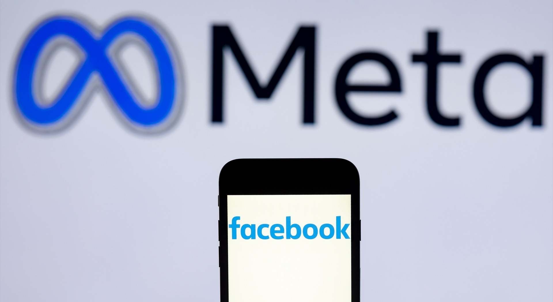 Móvil con el logo de Facebook en la pantalla y de fondo el de Meta