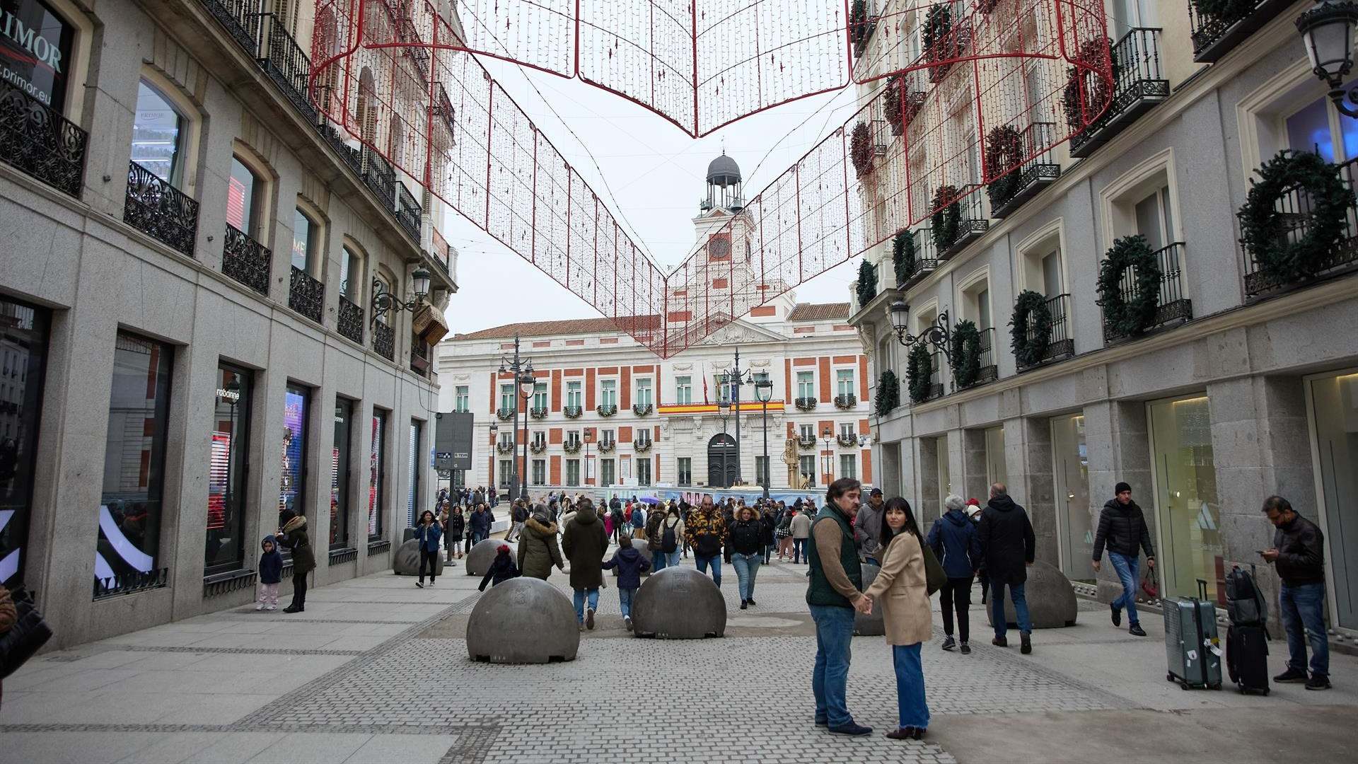 Varias personas en una calle comercial frente a la remodelada y peatonalizada Puerta del Sol