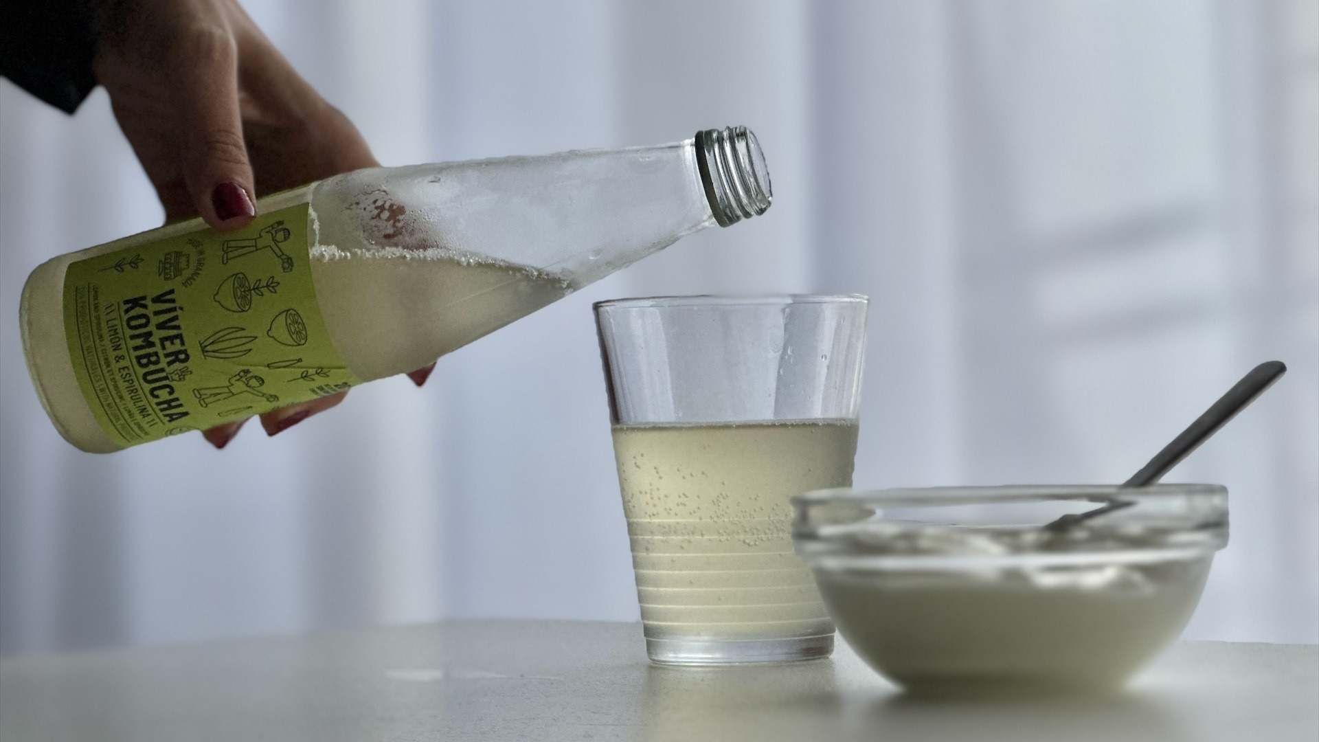 Persona sirviendo de una botella a un vaso kombucha junto a un yogur