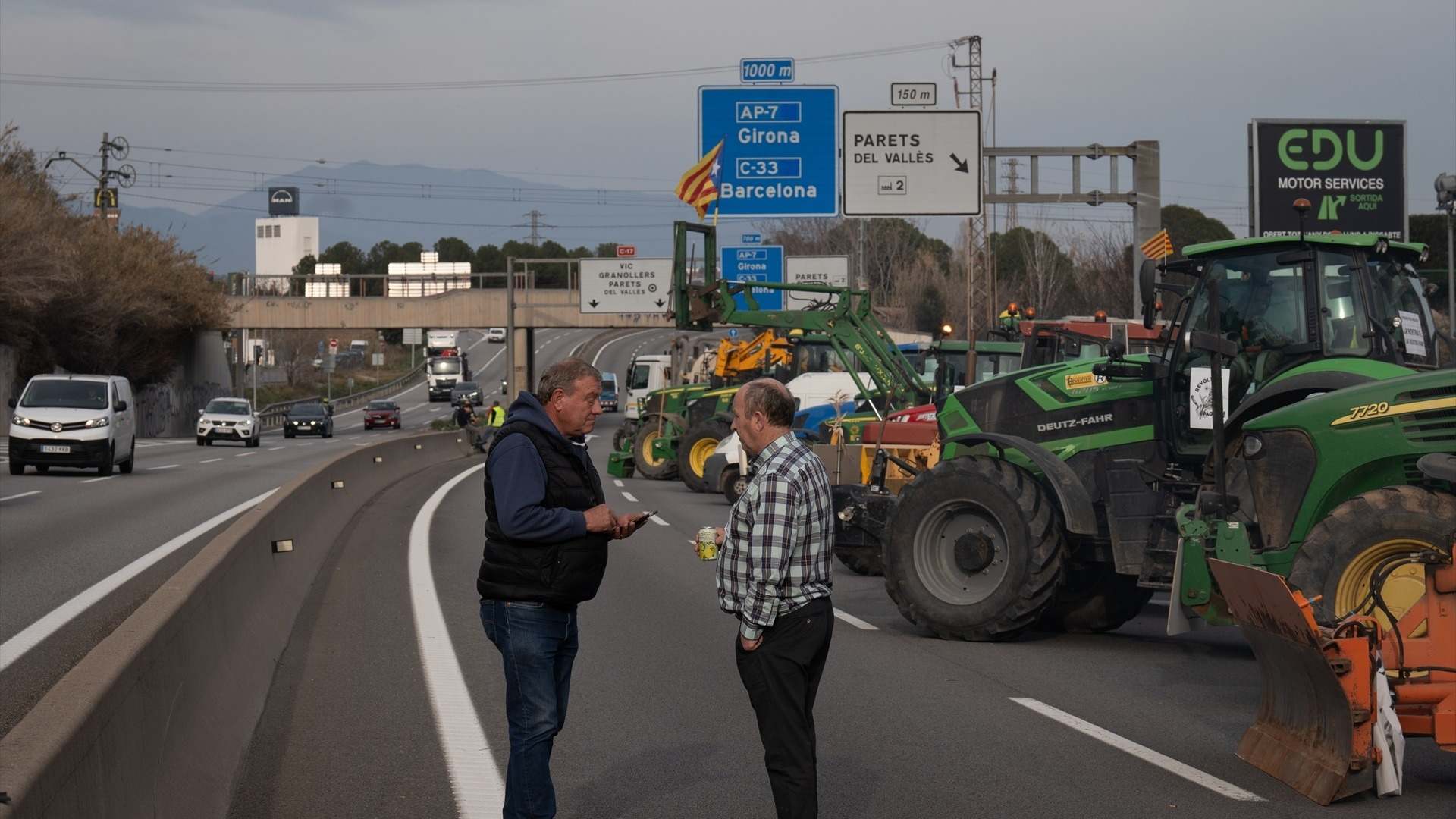 Varias personas entre los tractores que han cortado la carretera C-17